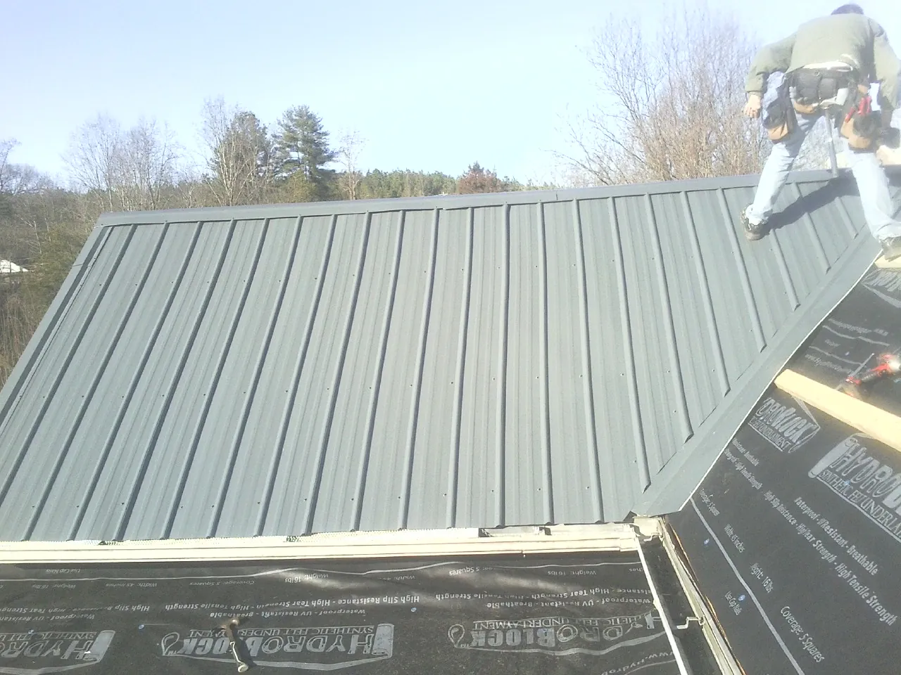 Crew installing dark green standing seam panels over synthetic underlayment in Alton Bay