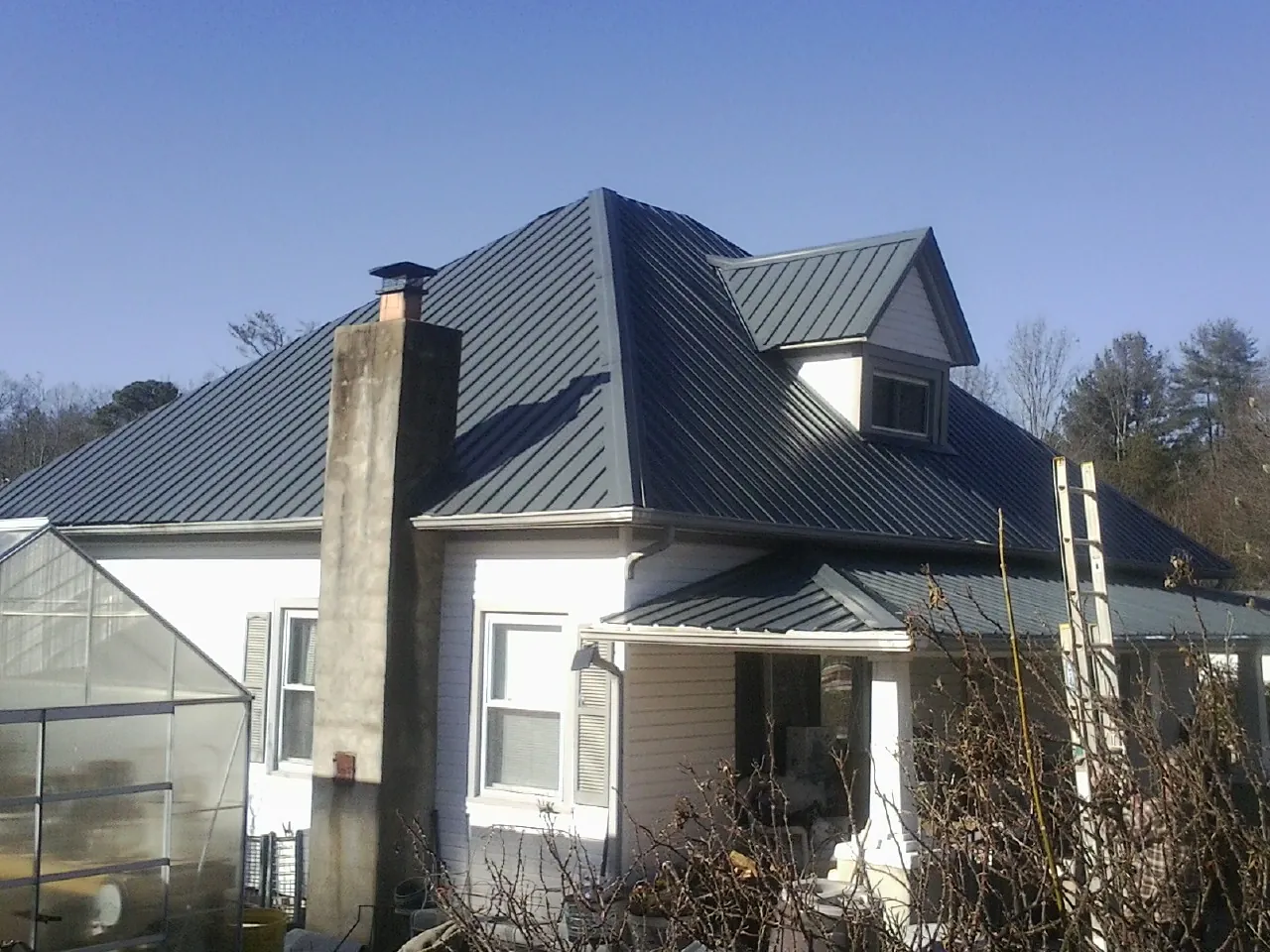 Dark blue standing seam metal roof on a white farmhouse with dormer — Slate & Tile Roof Repair by Roofing Brothers in Alton Bay