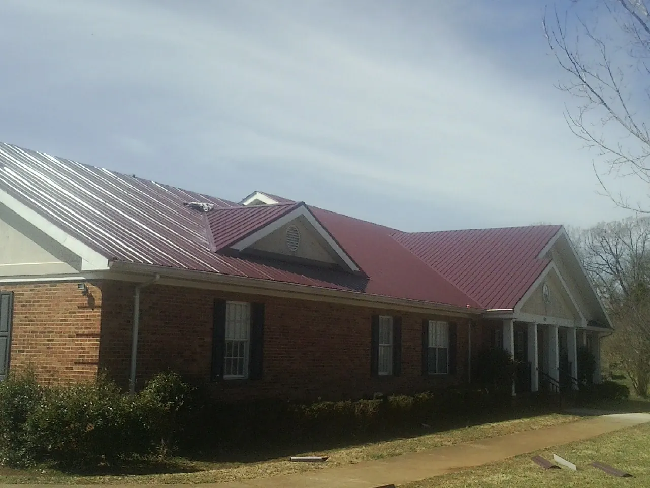 Red metal roof with gabled entries on a long brick building, from a Hail Damage Roof Repair job in Alton Bay