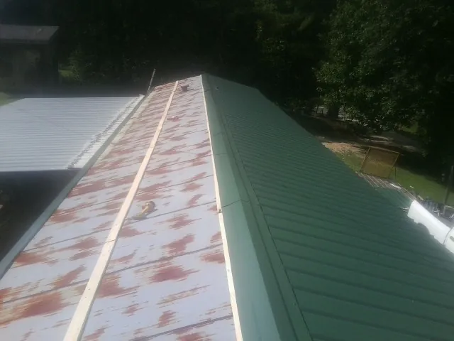 Old rusted panels beside newly installed green metal roofing — Wind Damage Roof Repair by Roofing Brothers in Alton Bay