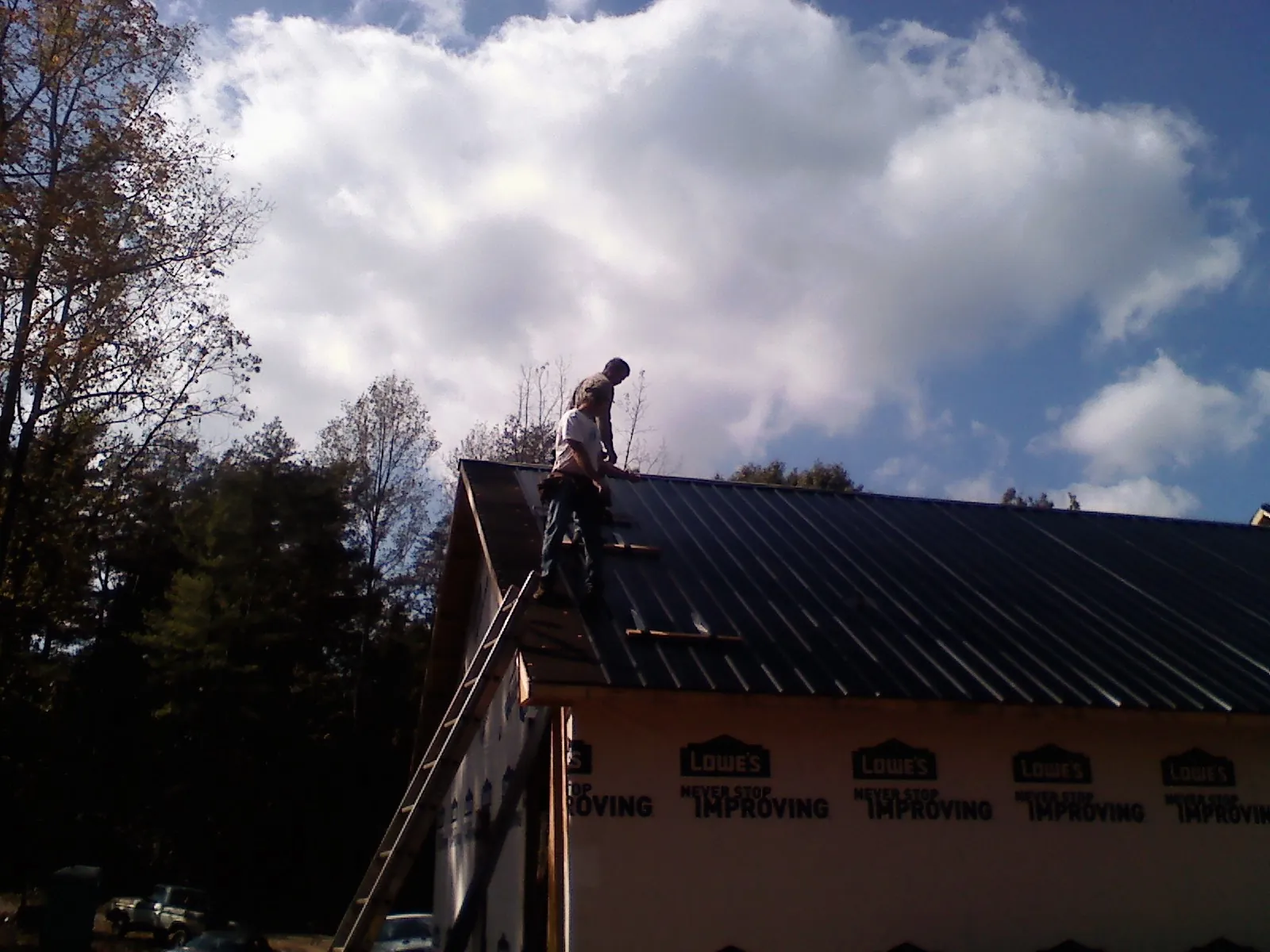 Roofer fastening dark metal panels high against a cloudy sky, from a Roof Inspection job in Alton Bay
