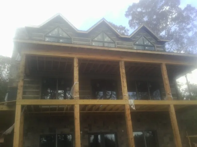 Dormers and porch framing on a large log home under construction — Roof Coating work by our crew in Alton Bay