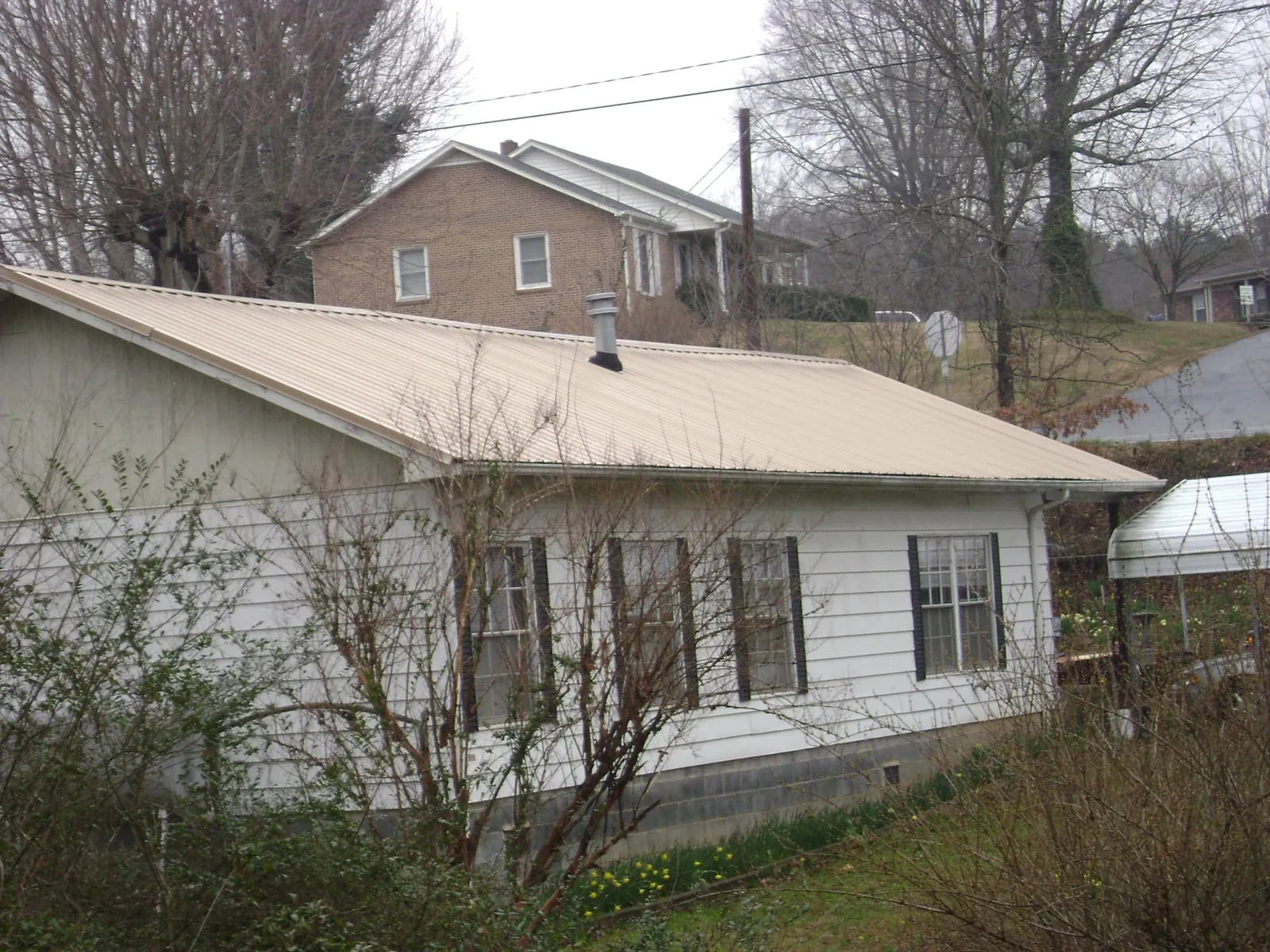 Tan metal roof on a white sided house set into a hillside — Commercial Roofing by Roofing Brothers in Alton Bay