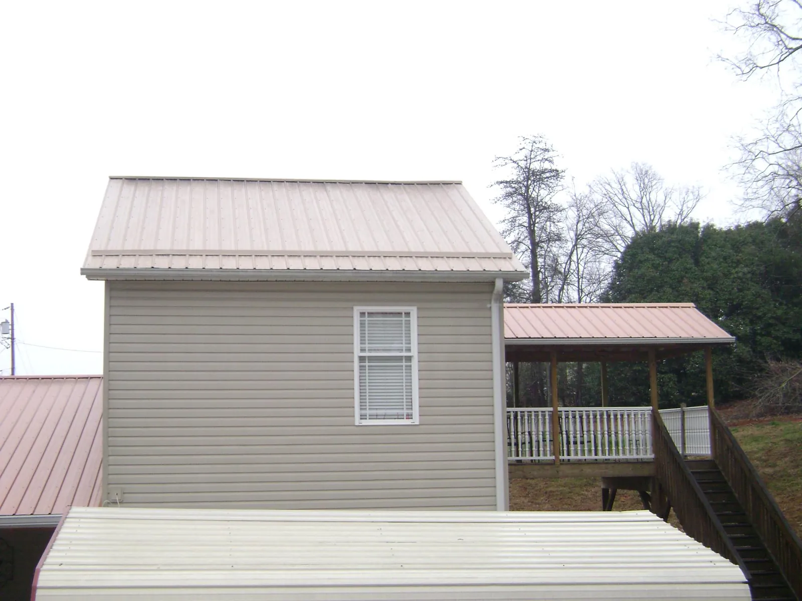 Tan metal roofs on a two story addition and attached porch, from a Roof Replacement job in Alton Bay